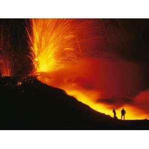  Two Scientists Stand Next to Lava and Spark Spewing Mount 